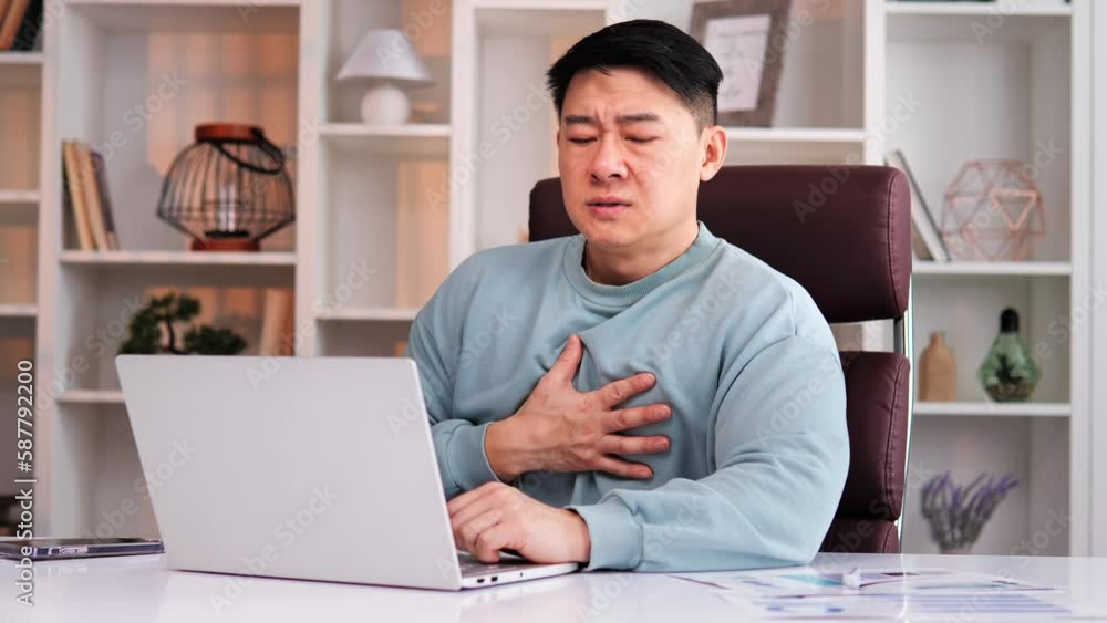 Chinese freelance businessman feeling unwell experiencing panic attack having difficulty breathing, accompanied by chest pain. Man touches chest in attempt to soothe himself while alone in office. Chinese freelance businessman feeling unwell experiencing panic attack having difficulty breathing, accompanied by chest pain. Man touches chest in attempt to soothe himself while alone in office.