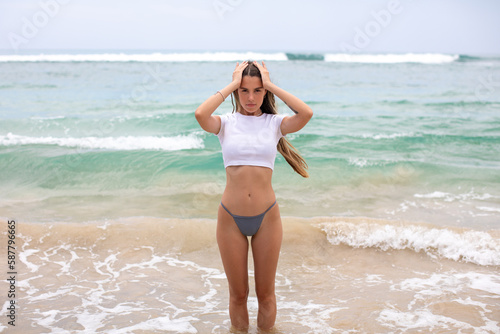 Beautiful young woman in a white cropped t-shirt comes out of the ocean. © kanashkin