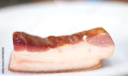 a piece of meat on a plate. piece of bacon with selective focus on white. bacon on white background. pork on white background. slice of bacon.