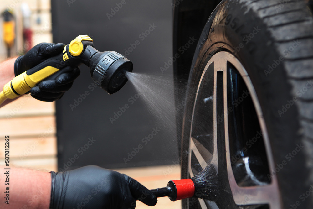 Cleaning the wheels of the car. The concept of a car wash in close-up. Car wash worker sprays cleaning agent.