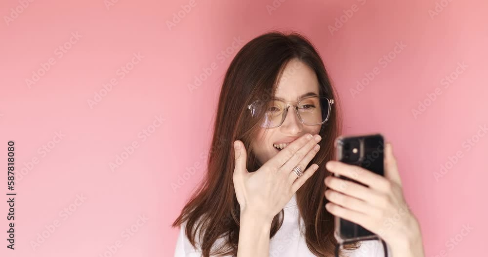 Brunette woman in eye glasses look surprised wow hold using mobile phone on pink background. Girl look on smartphone, cover mouth and doing winner gesture. Girl found out great big win news, sales. Brunette woman in eye glasses look surprised wow hold using mobile phone on pink background. Girl look on smartphone, cover mouth and doing winner gesture. Girl found out great big win news, sales.