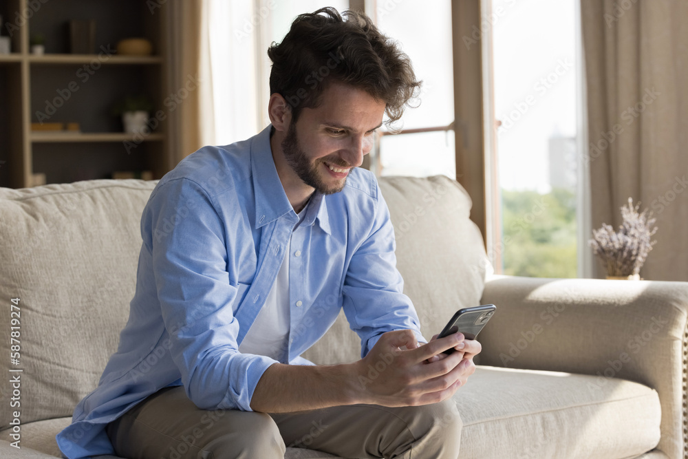 Joyful happy handsome young man using online application, media service on smartphone, enjoying connection, Internet communication at home, holding mobile phone, looking at screen, smiling Joyful happy handsome young man using online application, media service on smartphone, enjoying connection, Internet communication at home, holding mobile phone, looking at screen, smiling