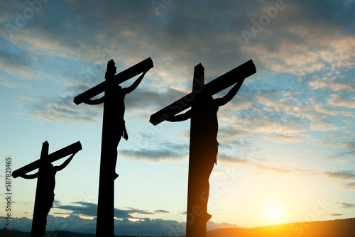Fototapeta Silhouette of the crucified Jesus Christ on the cross along with other people on background of sunset sky
