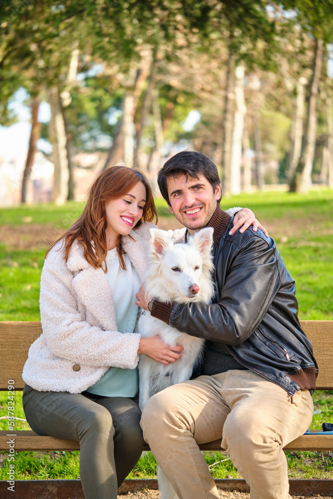 Young caucasian couple petting their dog sitting on a bench in a park. Family. Young caucasian couple petting their dog sitting on a bench in a park. Family.