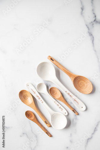Wooden and ceramic measuring spoons sit on a white marble surface