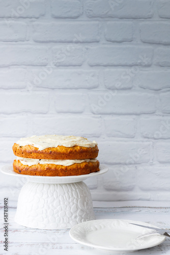 Carrots cake with cream cheese in front of a white brick wall