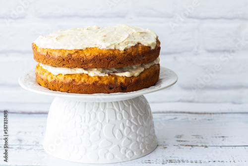 Carrots cake with cream cheese in front of a white brick wall