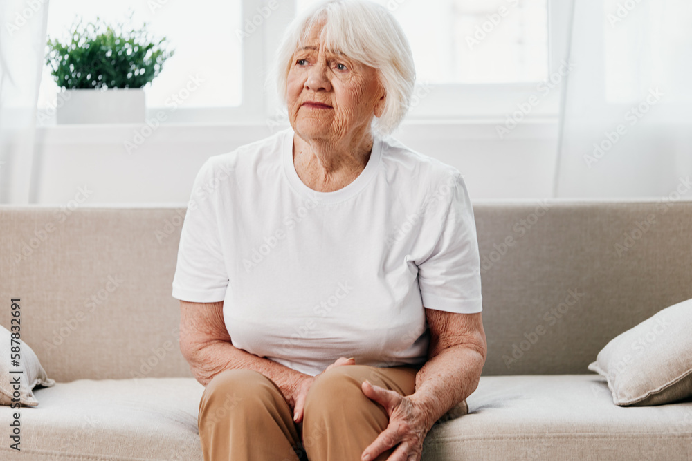 Elderly woman severe pain in her leg sitting on the couch, health