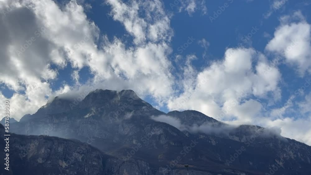 Low-hanging clouds stretch through powerful mountains against a cloudy blue sky Low-hanging clouds stretch through powerful mountains against a cloudy blue sky