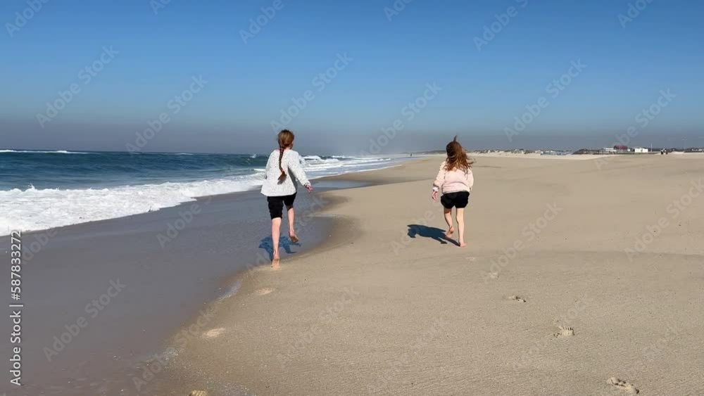 Children run along the coast of the Pacific Ocean. Two little sisters are playing with the waves on the beach of the Atlantic Ocean. Family time or vacation concept. 4K resolution video