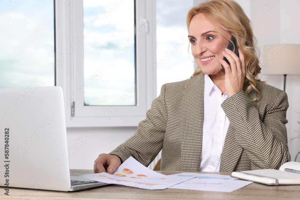 Lady boss talking on smartphone near laptop in office. Successful businesswoman Lady boss talking on smartphone near laptop in office. Successful businesswoman