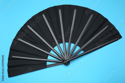 Stylish black hand fan on light blue background  top view