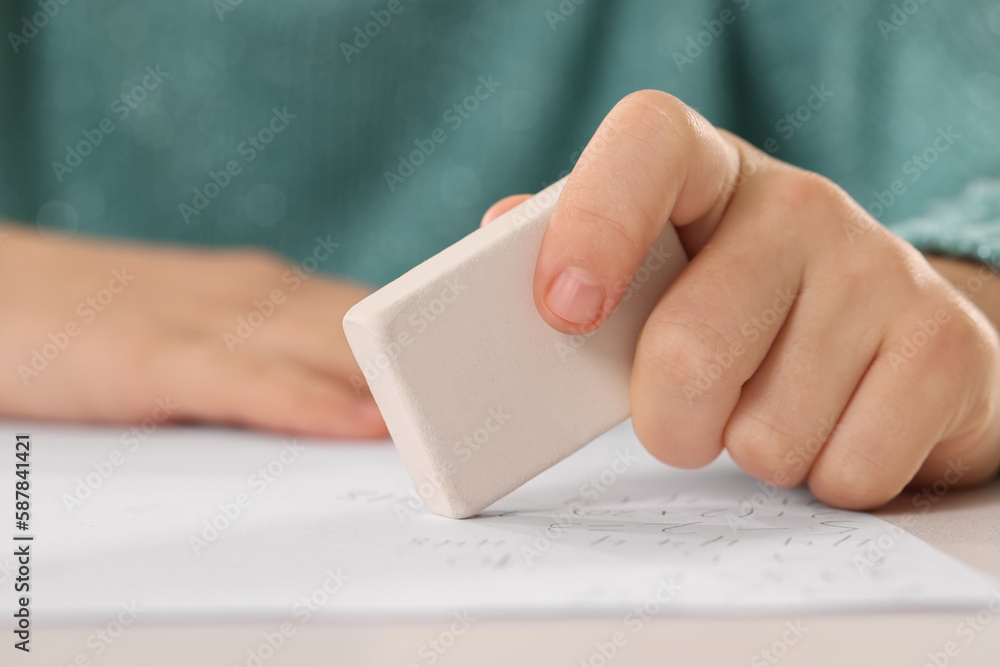 Girl erasing mistake in her homework at white desk, closeup Girl erasing mistake in her homework at white desk, closeup