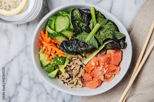 Poke bowl of raw fish, brown rice, cucumber, carrots, avocado, greens and sesame seeds  photo