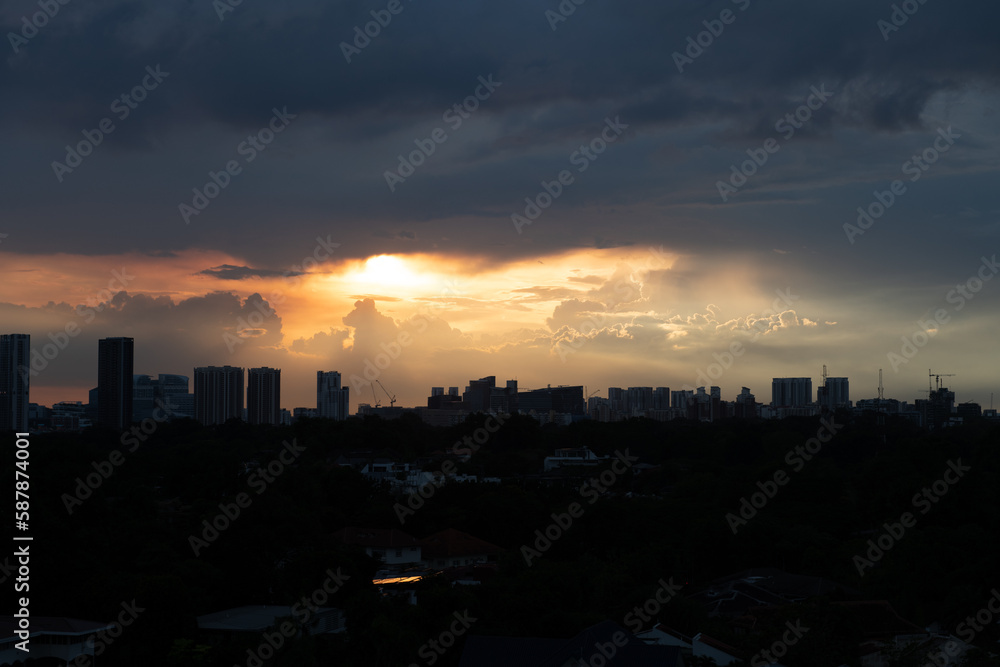Naklejka premium Warm sunset after rain with dark clouds above and silhouette of tall buildings and houses in foreground
