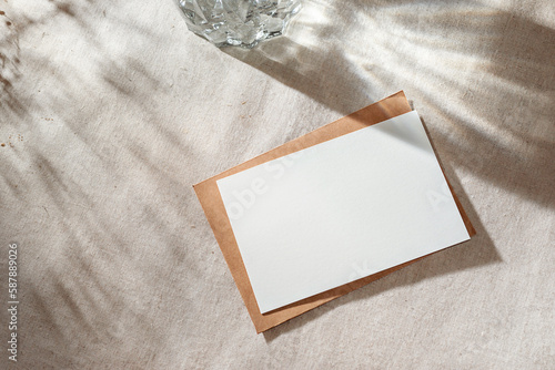 Empty paper card with mock up copy space on beige table surface with aestethic sunlight shadows, invitation or greeting card, branding template photo