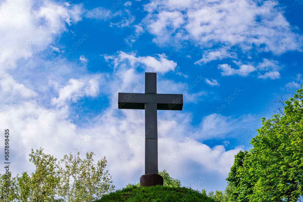 Christian cross on a mound against a blue sky with white clouds. Christian symbol. Religion and culture. Ukrainian Orthodox Church. Catholicism and Protestantism. Place of crucifixion. Easter.