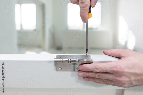 Worker installs a door hinge on a door using a screwdriver. Screw tightening. Repair in the house. Door installation. Close-up. photo
