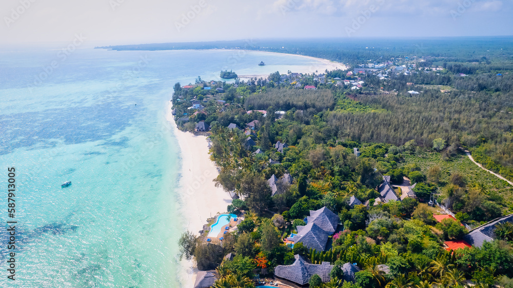 Set against a beautiful blue sky with fluffy clouds on a sunny summer day, Zanzibar Island's tropical beach is a sight to behold. The white sand, palm trees, and crystal-clear turquoise waters combine
