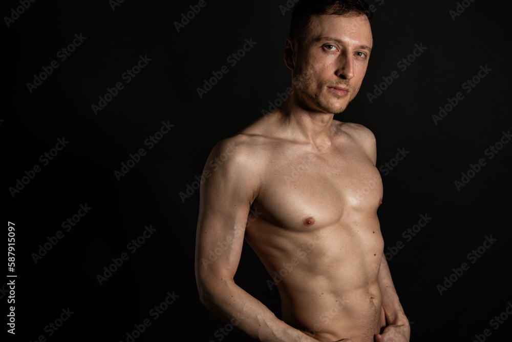 Adult attractive man with a beautiful body posing in the studio. Black background.