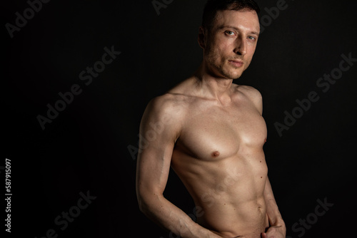 Adult attractive man with a beautiful body posing in the studio. Black background.