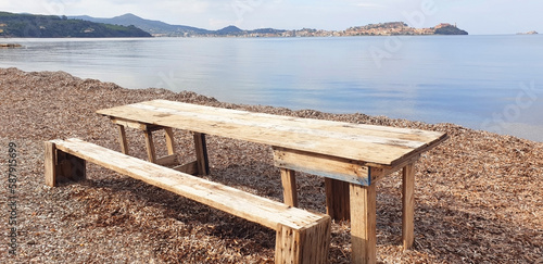 Wooden bench and table by the sea against the backdrop of the city of Portoferraio, Elba island. Panorama.