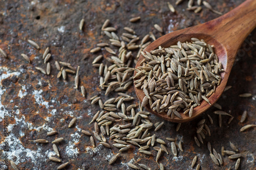Cumin seeds in wooden spoon on a textured background
