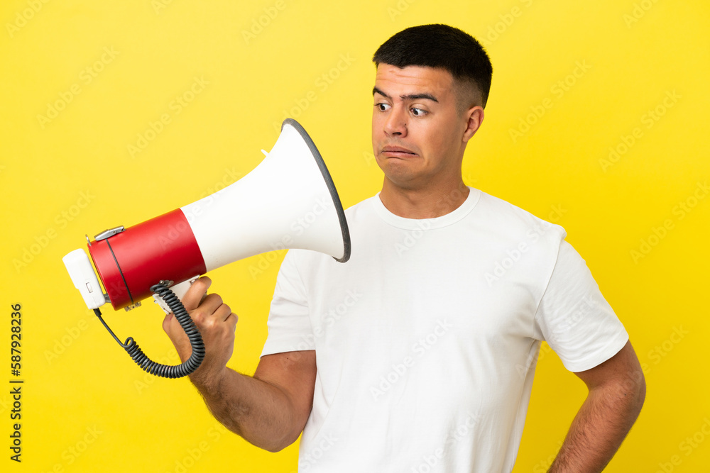 Young handsome man over isolated yellow background holding a megaphone with stressed expression Young handsome man over isolated yellow background holding a megaphone with stressed expression