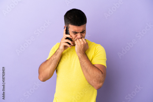 Young handsome man using mobile phone over isolated purple background having doubts