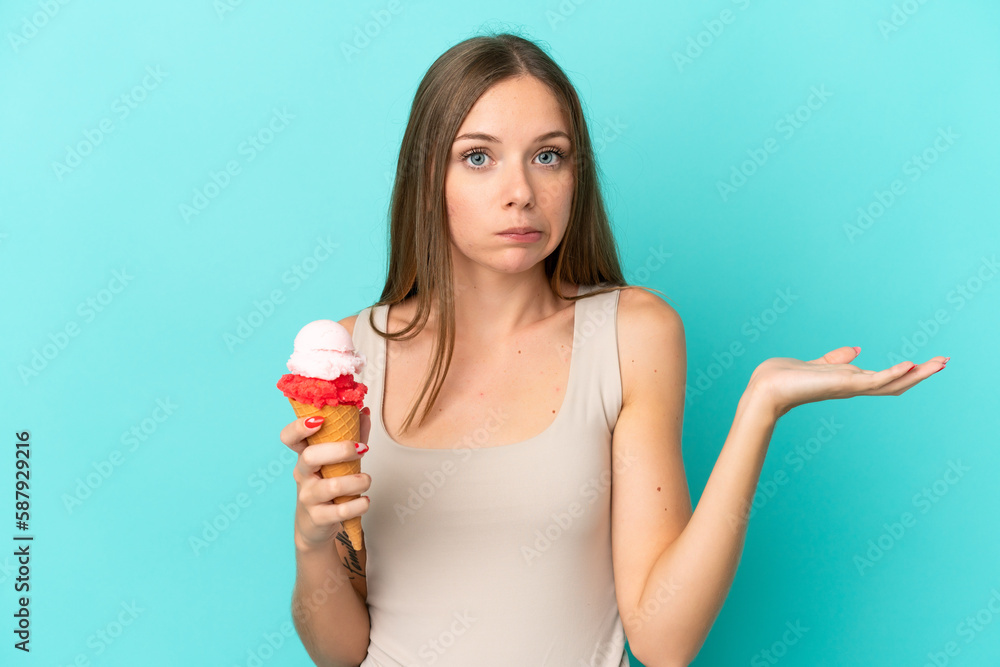 Young Lithuanian woman with cornet ice cream isolated on blue background having doubts while raising hands Young Lithuanian woman with cornet ice cream isolated on blue background having doubts while raising hands