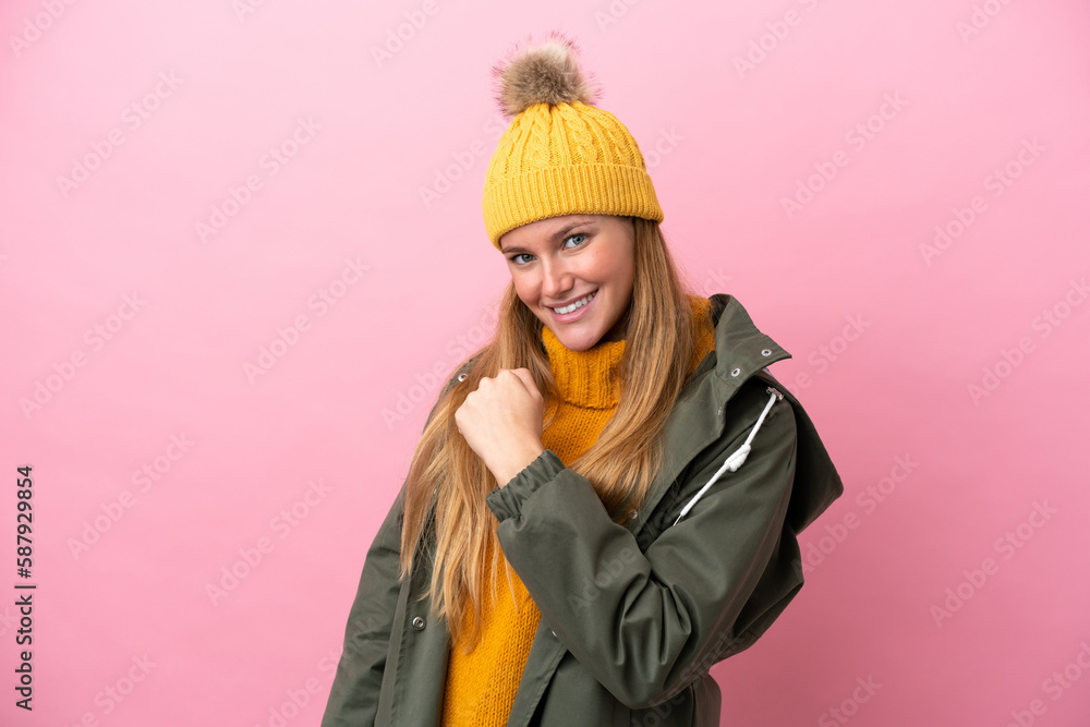 Young blonde woman wearing winter jacket isolated on pink background celebrating a victory Young blonde woman wearing winter jacket isolated on pink background celebrating a victory