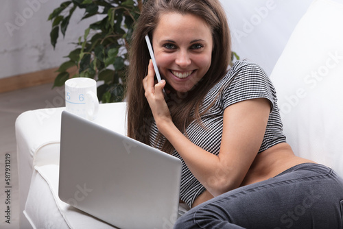 Young woman on couch, half-lying with laptop, phone delivering f