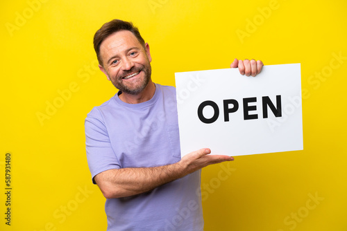 Middle age caucasian man isolated on yellow background holding a placard with peace symbol with happy expression © luismolinero