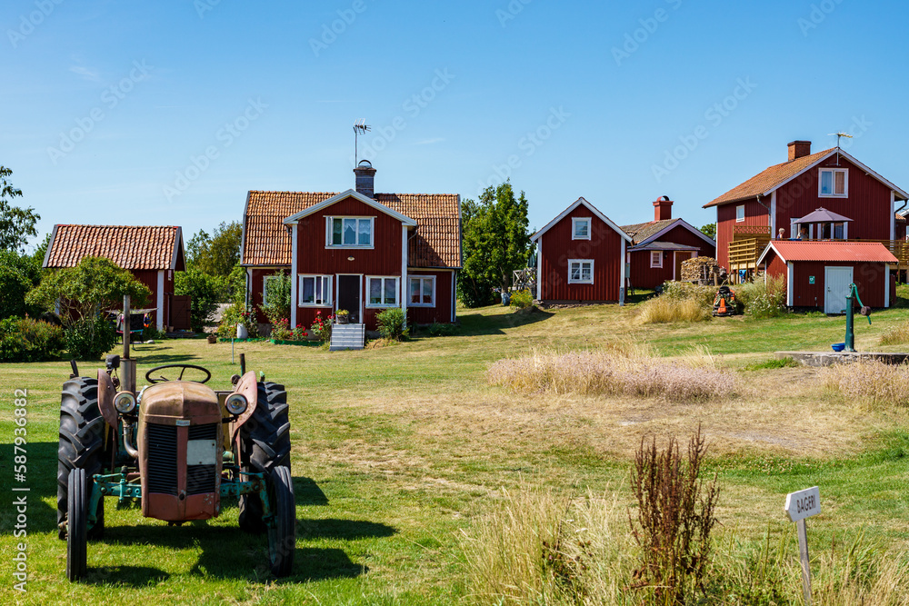 Obraz premium An old tractor, red houses and a communal hand water pump in a small village on the island of Harstena in the Gryt archipelago in the Baltic Sea