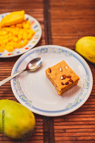 Close up of mango dry cake topped with chopped almonds. A single cake piece served with freshly cut mango pieces. Wholesome and nutritious eating and cake recipe concept vertical image. photo
