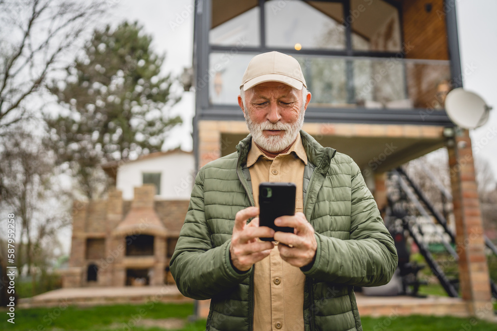 One senior man stand in front of tiny house in day use smart phone
