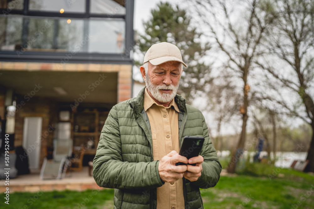 One senior man stand in front of tiny house in day use smart phone One senior man stand in front of tiny house in day use smart phone