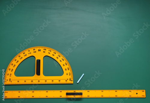 Protractor, ruler and chalk on green chalkboard, flat lay. Space for text