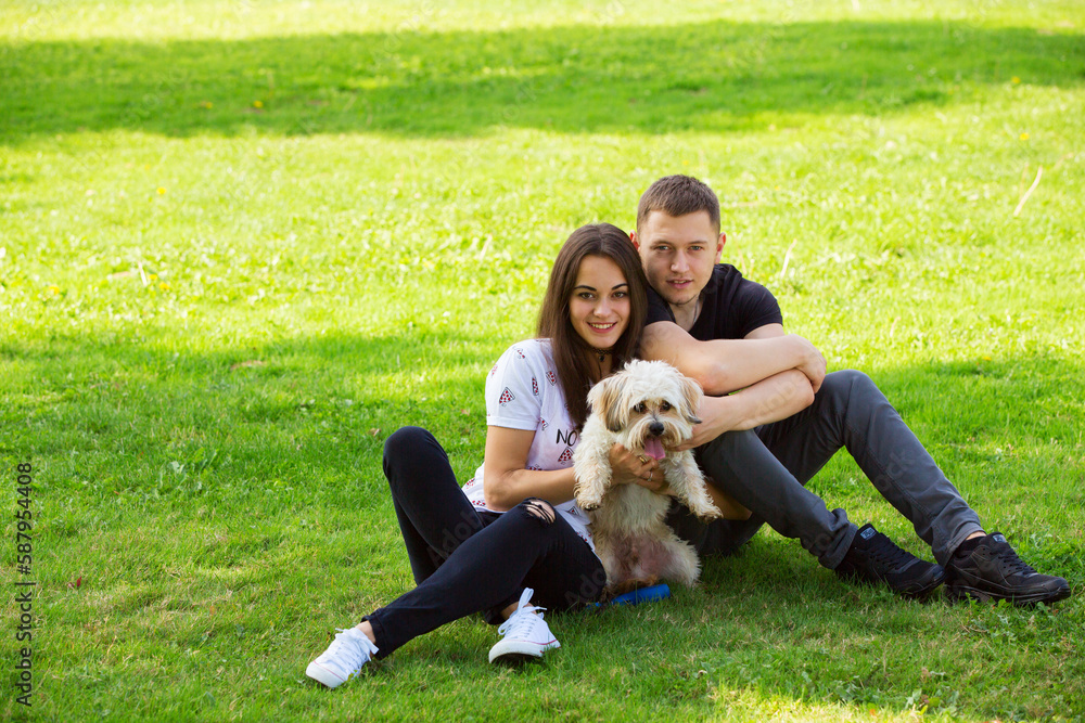 Obraz premium Young couple with puppy. Portrait of attractive happy smiling young woman and man holding cute little dog, summer park outdoor.