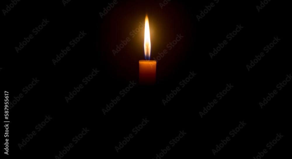 A single burning candle flame or light is glowing on an orange candle on black or dark background on table in church for Christmas, funeral or memorial service with copy space. A single burning candle flame or light is glowing on an orange candle on black or dark background on table in church for Christmas, funeral or memorial service with copy space.