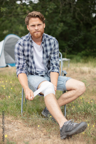 man put bandage on painful knee during camping © auremar