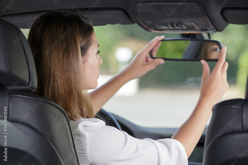 attractive female student adjusting car rear-view mirror during driving lesson attractive female student adjusting car rear-view mirror during driving lesson