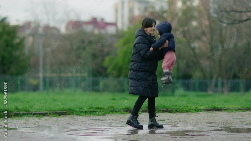 Woman and her daughter walking through puddle, jumping and splashing water. Mother and child having fun at rainy weather. Woman and her daughter walking through puddle, jumping and splashing water. Mother and child having fun at rainy weather.