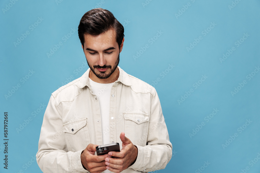 Portrait of a brunette man talking on the phone mobile and internet online, smile with teeth surprise and happiness, on a blue background in a white T-shirt, copy space