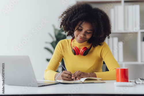 Beautiful American women student studying online takes notes on her laptop to gather information about her work smiling face and a happy study posture.