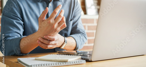 close up employee man massage on his hand and arm for relief pain from hard working on the desktop table at hoe office for stiff or cramp symptom or carpal tunnel syndrome concept