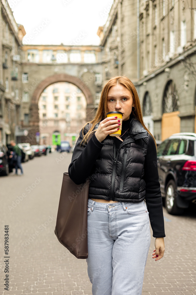 Young woman in black jacket and jeans with coffee on the street urban fashion