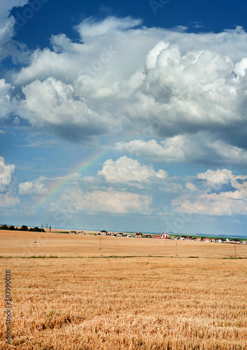 panorama of mown stubble, cumulus clouds and rainbow, village and houses on t...