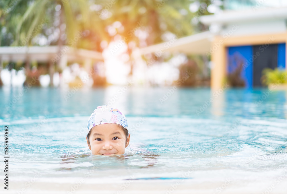 Asian child holiday relax or kid girl wearing swimsuit and cap on swimming pool and smile with happy fun in waterpark for learning swim to sport exercise on summer school or vacation travel at hotel