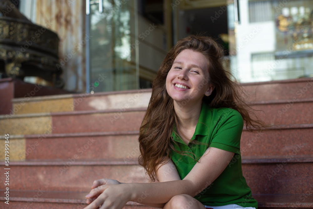 young beautiful woman is sitting on steps near hotel or new house, home and smiling young beautiful woman is sitting on steps near hotel or new house, home and smiling